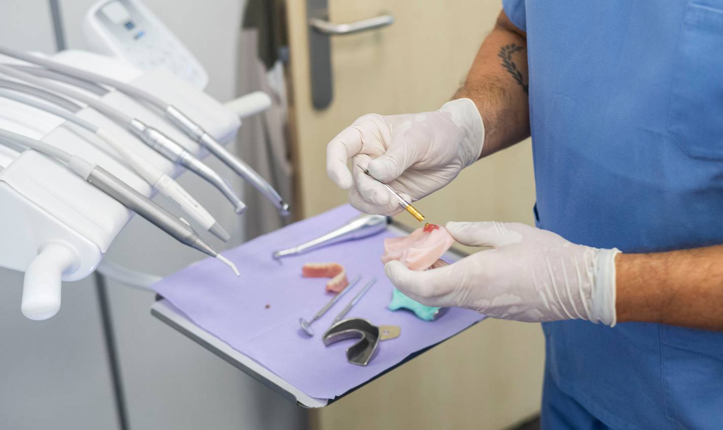 Profesional dental manipulando una prótesis en un entorno clínico, destacando el trabajo técnico y detallado en la preparación de tratamientos protésicos.